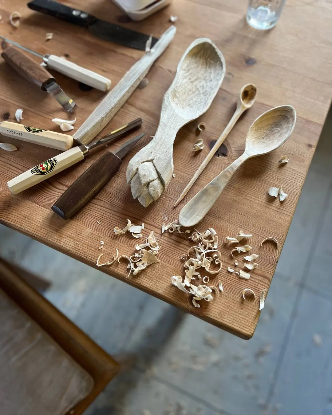 Geschnitzte Holzlöffel, Messer und Späne auf einem Werktisch